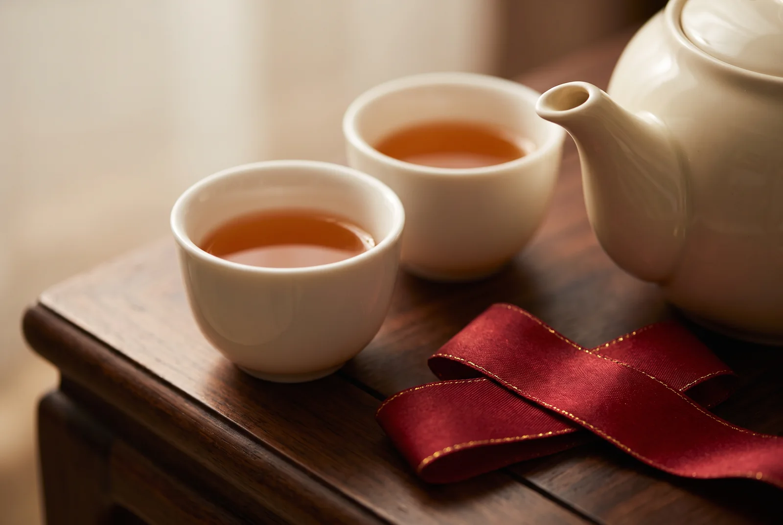 Two porcelain tea cups beside a red ribbon and teapot — AI-generated editorial illustration
