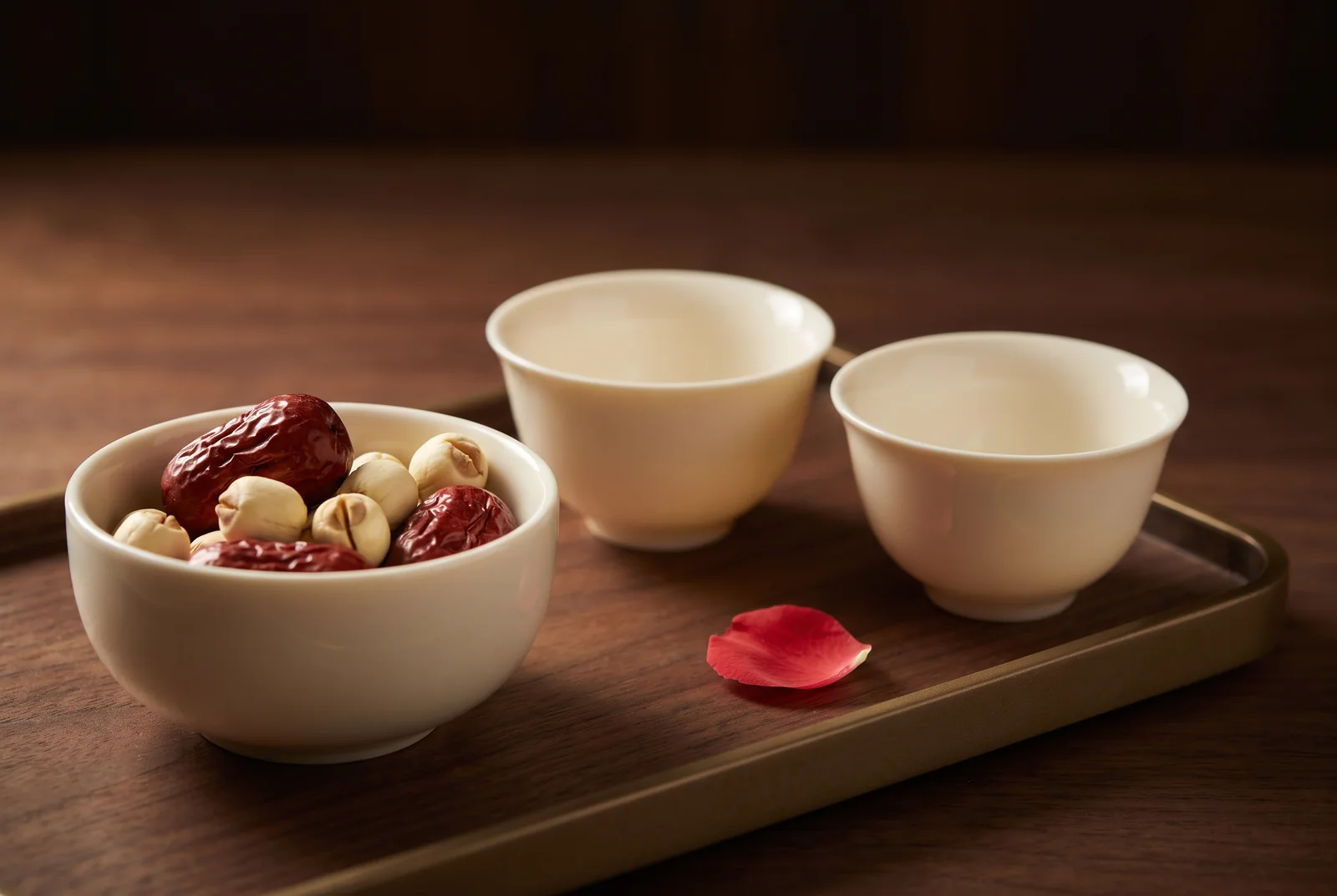 Red dates and lotus seeds beside plain tea cups — AI-generated editorial illustration