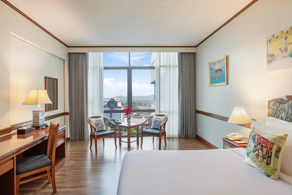 A hotel bedroom with a desk and table beside the window