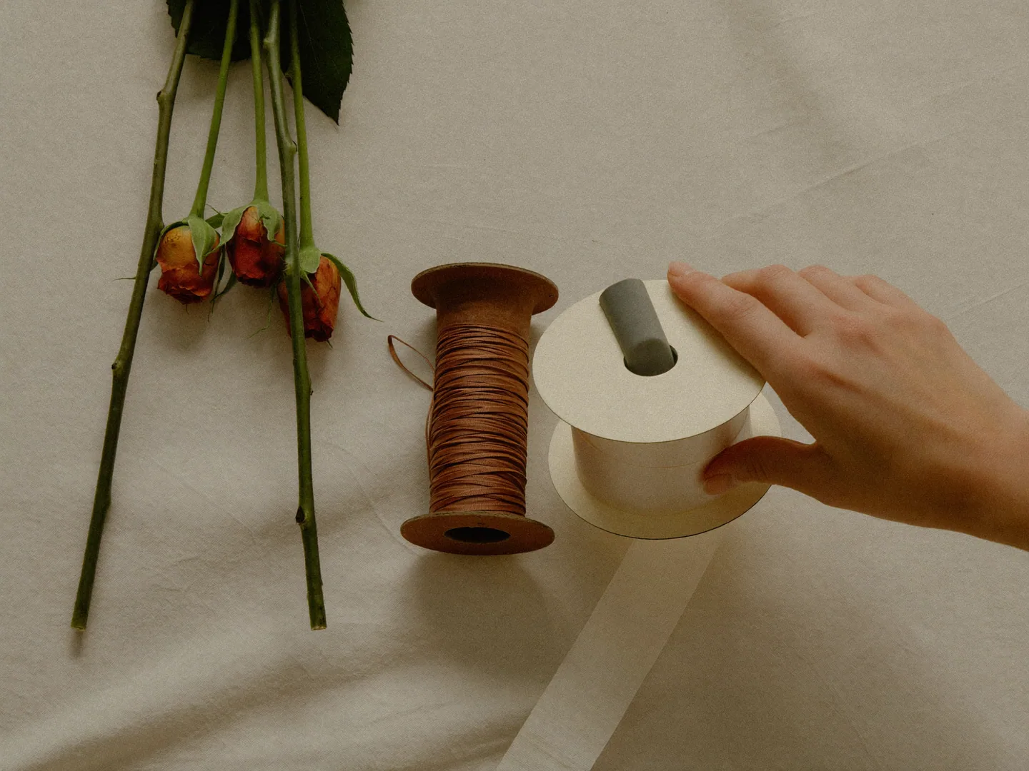 An illustrative hand comparing ivory and terracotta ribbon materials beside flowers