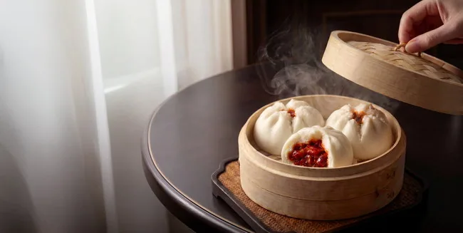A bun in a bamboo steamer with its filling visible