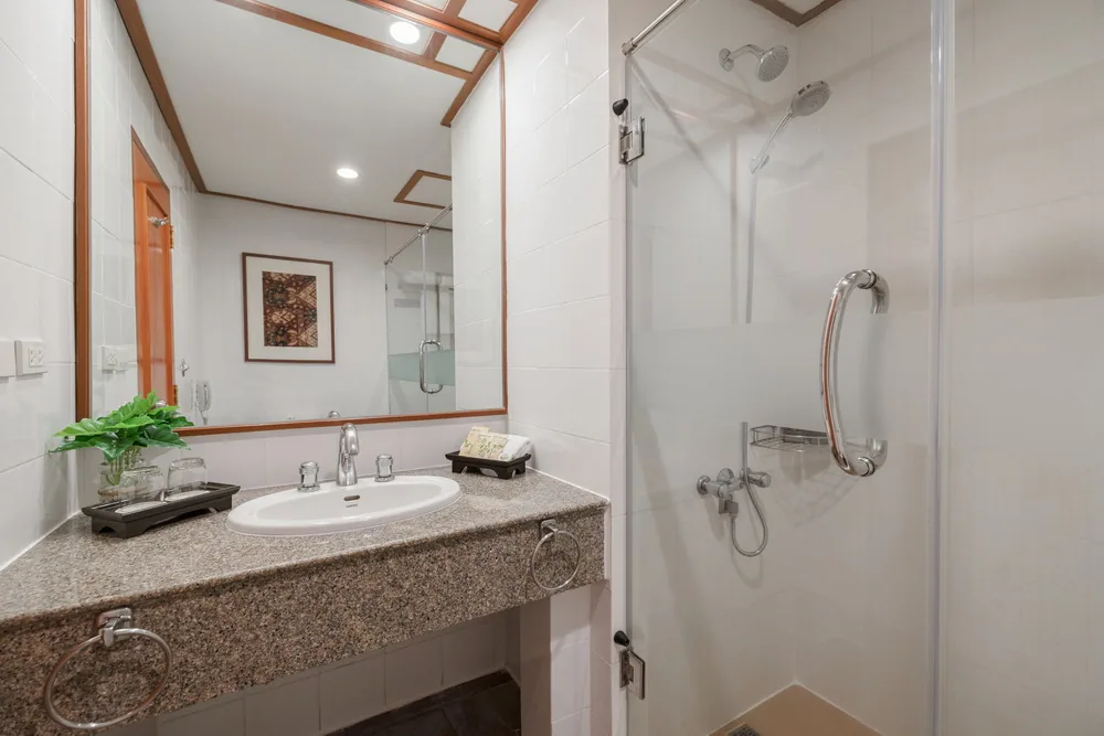 A hotel room bathroom with a basin, mirror and glass-enclosed shower