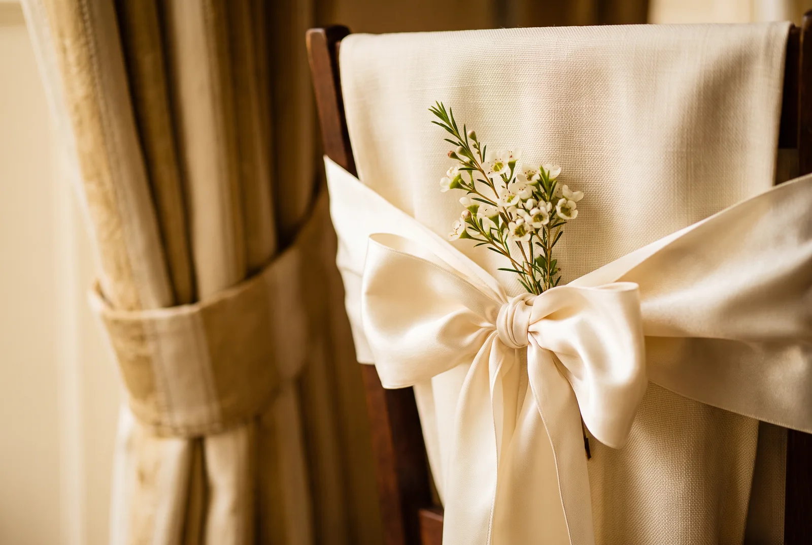 Ivory chair sash tied beside a small white floral sprig — AI-generated editorial illustration