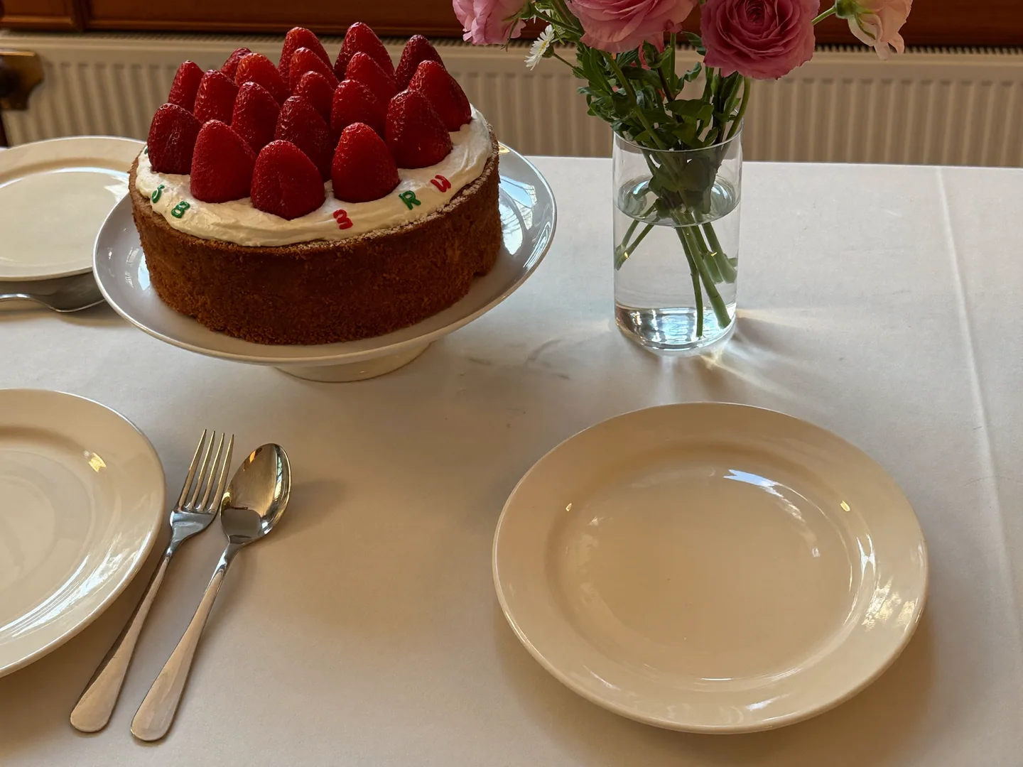 A celebration-planning concept with a strawberry cake, flowers and dessert plates