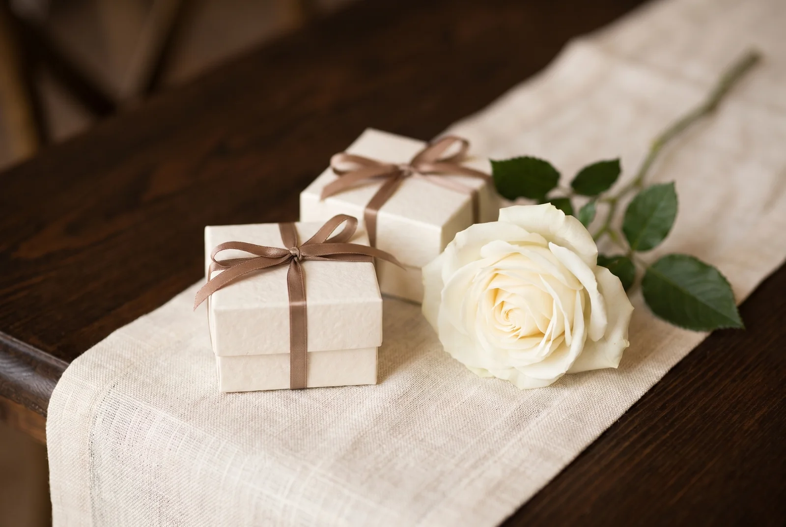 Small ivory favour boxes with bronze ribbons and a white rose — AI-generated editorial illustration